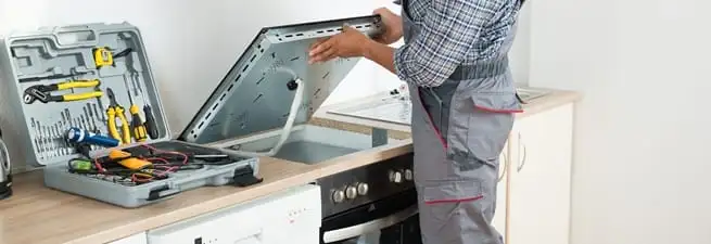 Cooktop repair technician lifting a built-in stovetop for service in Tulsa, OK