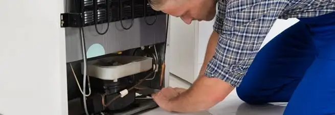 Refrigerator repair technician servicing the compressor and condenser area in Tulsa, OK