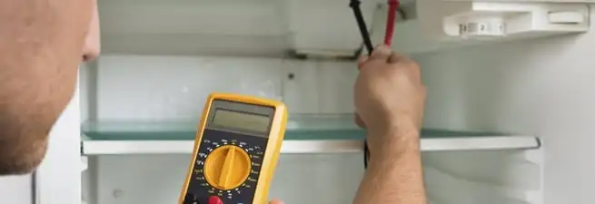 Refrigerator repair technician testing electrical components with a multimeter in Tulsa, OK