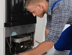 Refrigerator repair technician servicing the compressor and condenser area in Tulsa, OK